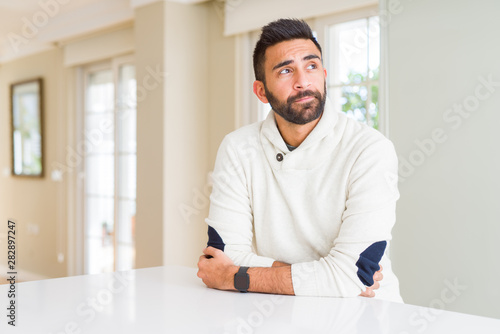 Handsome hispanic man wearing casual white sweater at home smiling looking side and staring away thinking. © Krakenimages.com
