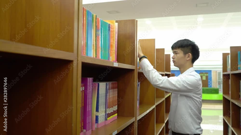 Young asian is walking between book shelf,choose books in the library,Concept educational. Young asian is walking between book shelf,choose books in the library,Concept educational.