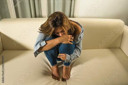 portrait of young sad and depressed girl crying desperate at home couch feeling broken heart suffering depression crisis and anxiety problem covering her face