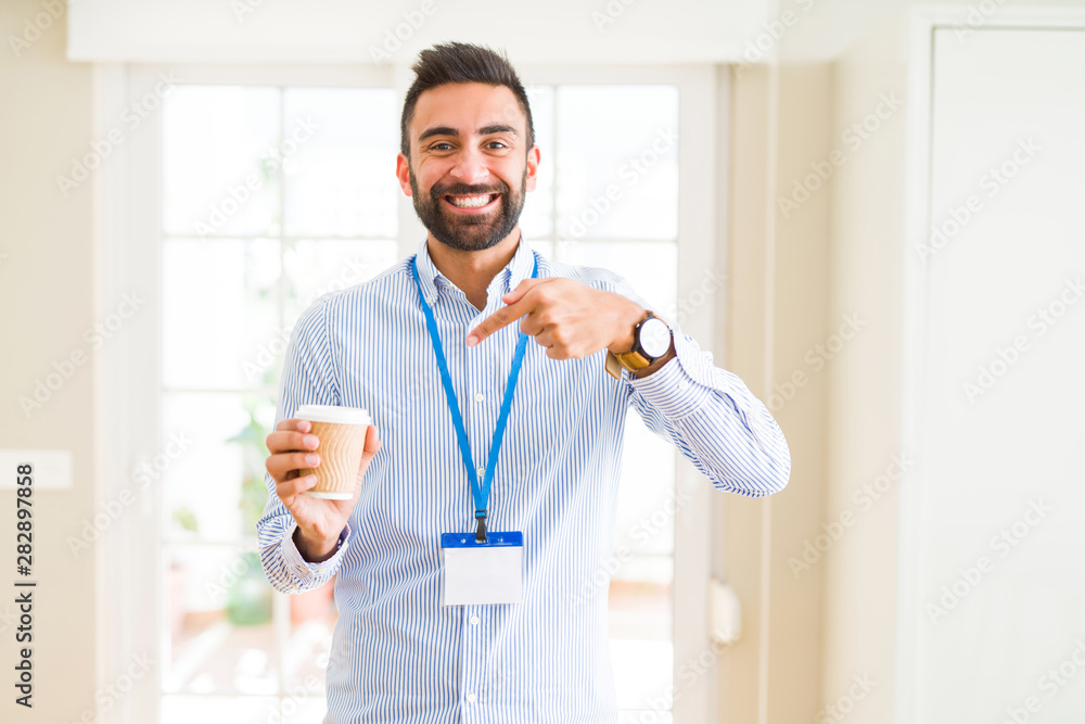 Handsome hispanic man wearing id card and drinking a cup of coffee very happy pointing with hand and finger Handsome hispanic man wearing id card and drinking a cup of coffee very happy pointing with hand and finger