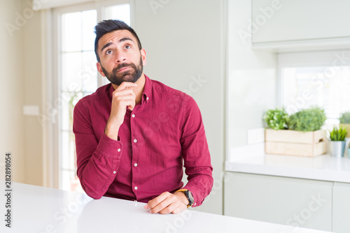 Handsome hispanic business man with hand on chin thinking about question, pensive expression. Smiling with thoughtful face. Doubt concept. © Krakenimages.com