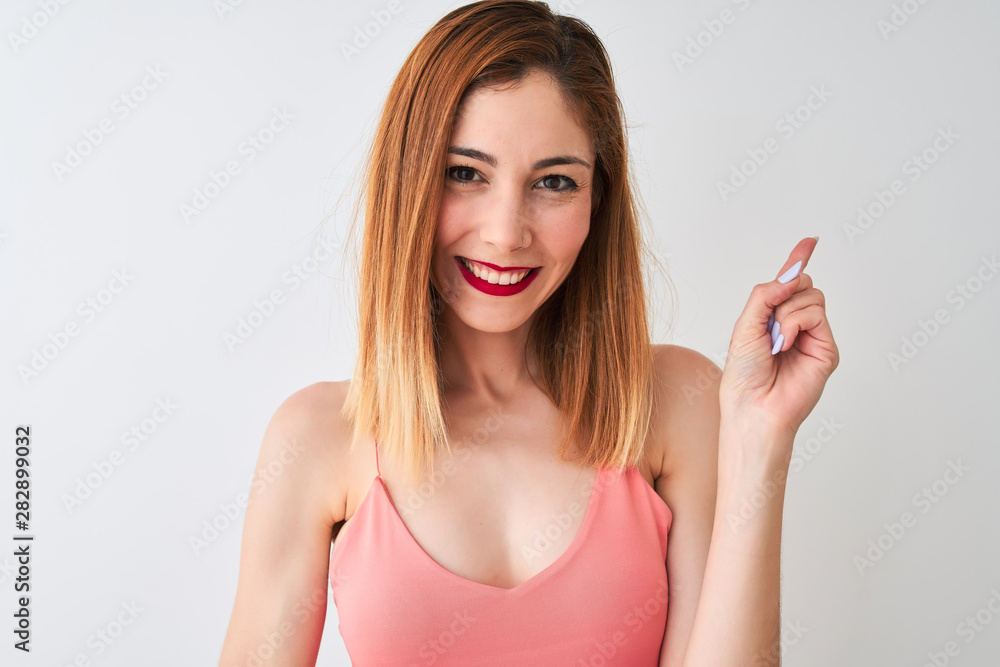 Beautiful redhead woman wearing casual pink t-shirt standing over isolated white background very happy pointing with hand and finger to the side Beautiful redhead woman wearing casual pink t-shirt standing over isolated white background very happy pointing with hand and finger to the side
