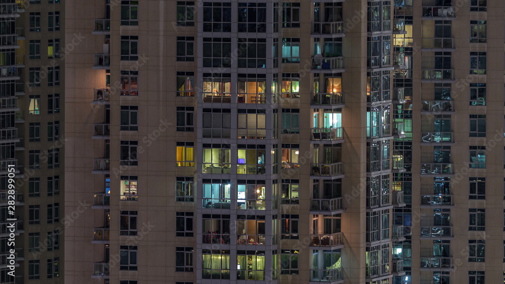 Windows of the multi-storey building with lighting inside and moving people in apartments timelapse.