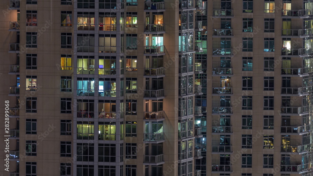 Windows of the multi-storey building with lighting inside and moving people in apartments timelapse.