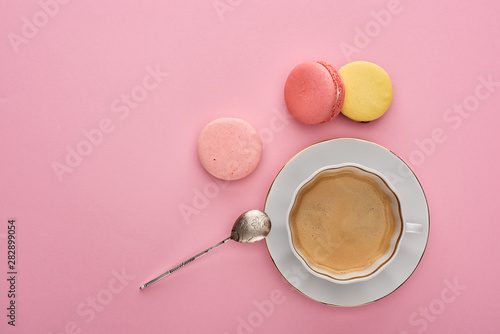 Top view of delicious French macaroons near coffee on pink background with copy space