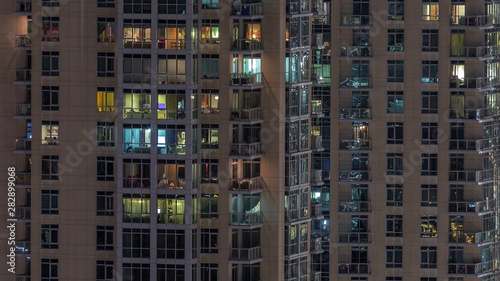 Windows of the multi-storey building with lighting inside and moving people in apartments timelapse.