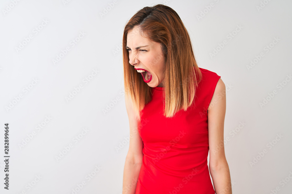 Redhead businesswoman wearing elegant red dress standing over isolated white background angry and mad screaming frustrated and furious, shouting with anger. Rage and aggressive concept. Redhead businesswoman wearing elegant red dress standing over isolated white background angry and mad screaming frustrated and furious, shouting with anger. Rage and aggressive concept.