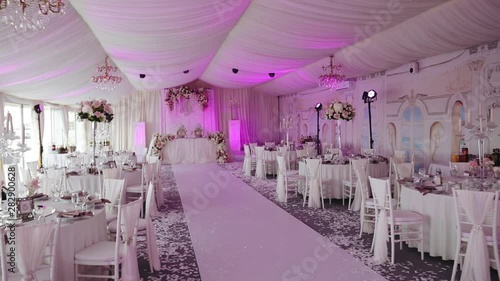 elegant banquet hall decorated in white style for wedding ceremony and lit with pink light in comfortable restaurant