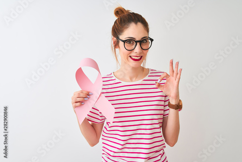 Beautiful redhead woman wearing glasses holding cancer ribbon over isolated white background doing ok sign with fingers, excellent symbol