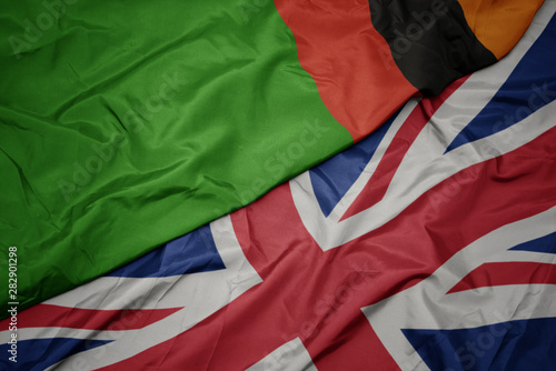 waving colorful flag of great britain and national flag of zambia.