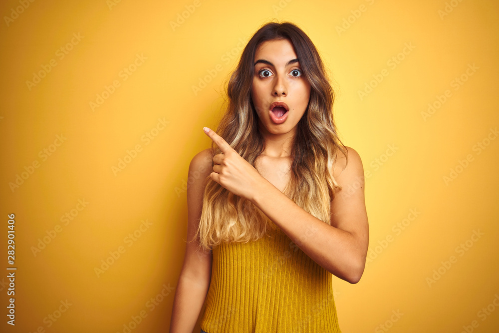 Young beautiful woman wearing t-shirt over yellow isolated background Surprised pointing with finger to the side, open mouth amazed expression. Young beautiful woman wearing t-shirt over yellow isolated background Surprised pointing with finger to the side, open mouth amazed expression.