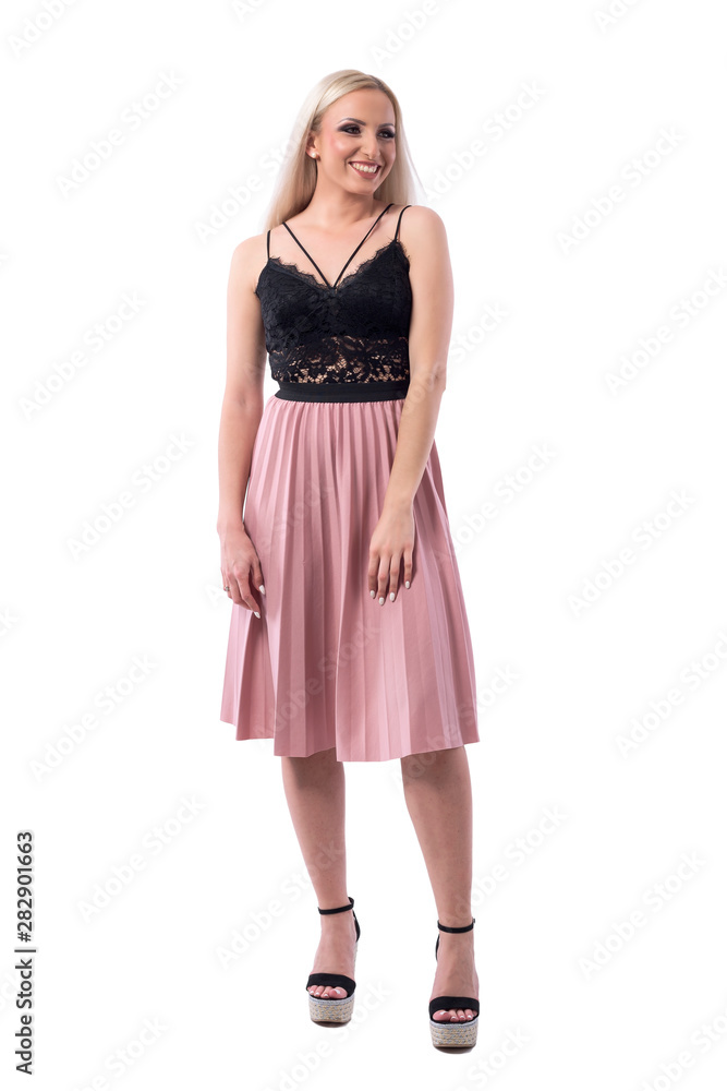 Cheerful young blonde woman in salmon color pleated skirt and lace top looking away. Full body isolated on white background. 