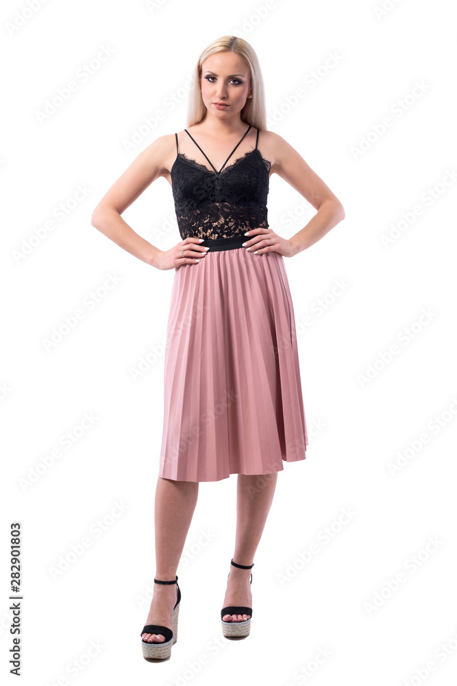 Displeased serious young blonde woman in elegant summer clothes with hands on hips looking at camera. Full body isolated on white background. 