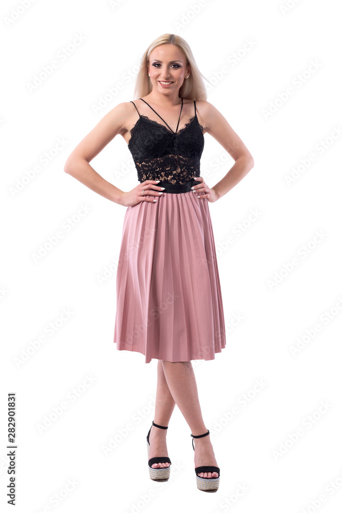 Cute pretty blonde woman in black lace top and salmon color skirt posing with arms on hips. Full body isolated on white background. 