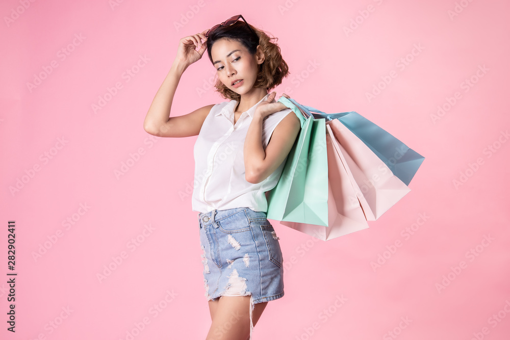 Asian pretty young woman walking over pink pastel background. She smiling and holding shopping bags. she nice-looking lovely attractive shine . Asian pretty young woman walking over pink pastel background. She smiling and holding shopping bags. she nice-looking lovely attractive shine .