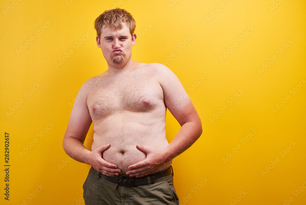 Huge funny young man with naked body touches big fat belly on yellow  background in studio. Concept of obesity, fast and junk food, sports,  liposuction, weight loss Stock Photo | Adobe Stock
