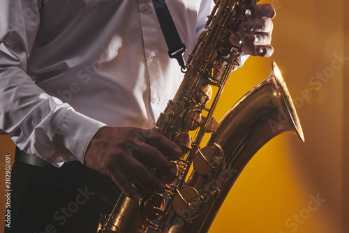 Portrait of professional musician saxophonist man in white shirt plays jazz music on saxophone, yellow background in a photo studio, side view