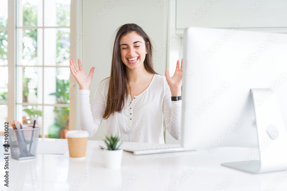 Beautiful young woman working using computer celebrating mad and crazy for success with arms raised and closed eyes screaming excited. Winner concept Beautiful young woman working using computer celebrating mad and crazy for success with arms raised and closed eyes screaming excited. Winner concept