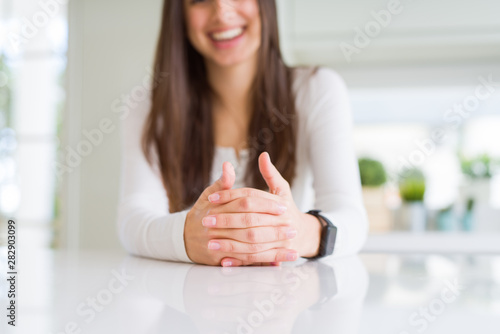 Close up of woman smiling with crossed hands over white table