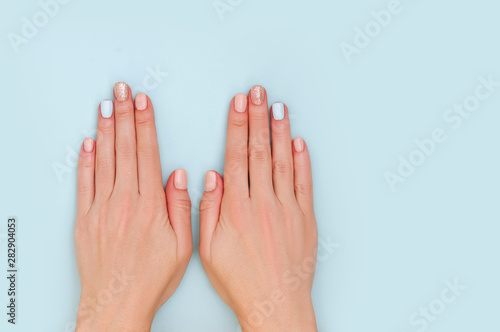 Woman's hands with pastel manicure on blue background with copy space.