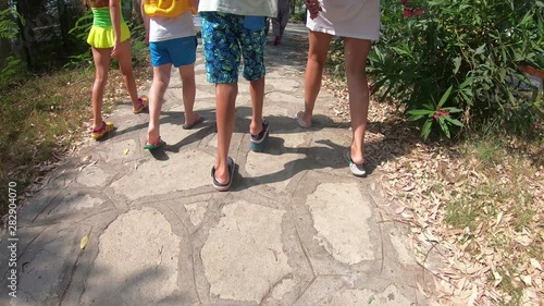 A short-legged baby is walking with friends.  A boy with foot disease in special shoes is walking along the road with friends. photo