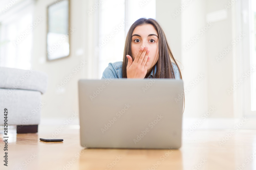 Beautiful young woman laying on the floor using laptop cover mouth with hand shocked with shame for mistake, expression of fear, scared in silence, secret concept Beautiful young woman laying on the floor using laptop cover mouth with hand shocked with shame for mistake, expression of fear, scared in silence, secret concept