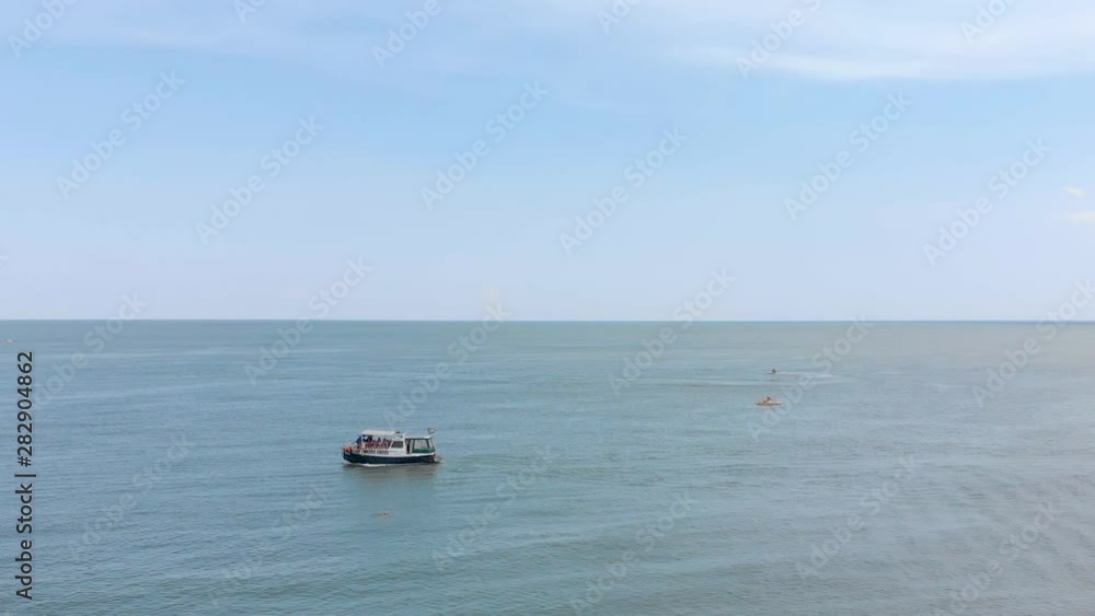 The boat sails on the sea. People sunbathe on the beach. Aerial view of beach and sea. Wave on the sea, ocean. Beach. Quadcopter. The boat sails on the sea. People sunbathe on the beach. Aerial view of beach and sea. Wave on the sea, ocean. Beach. Quadcopter.