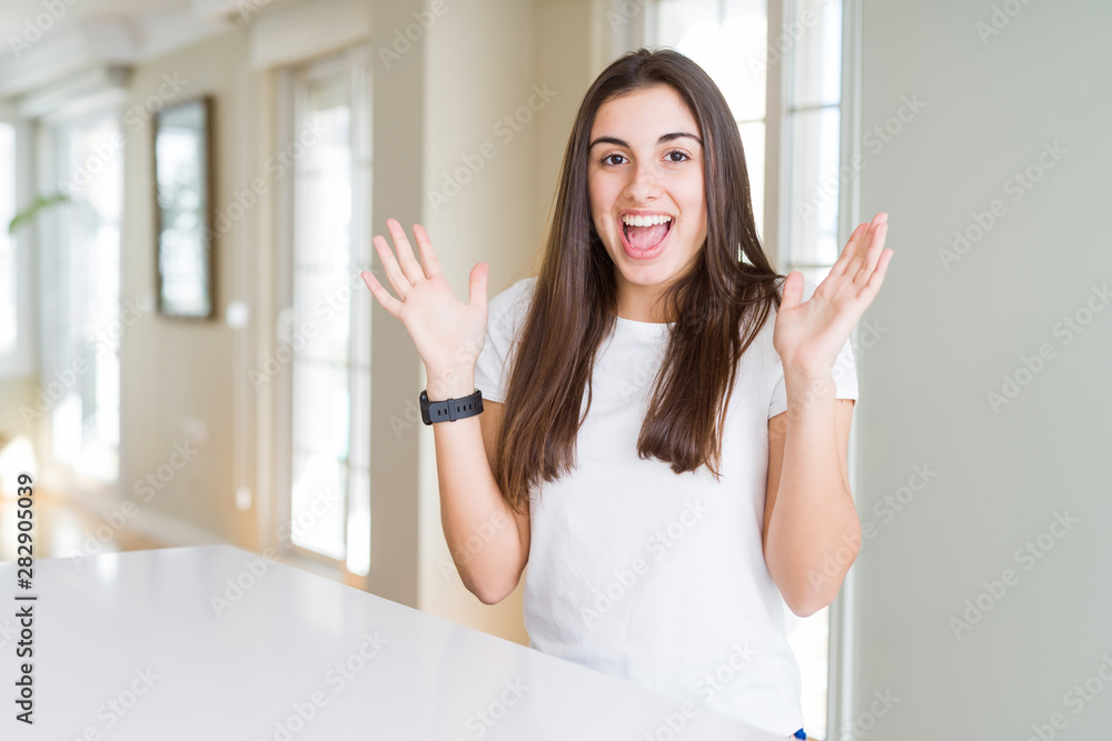 Beautiful young woman wearing casual white t-shirt celebrating crazy and amazed for success with arms raised and open eyes screaming excited. Winner concept Beautiful young woman wearing casual white t-shirt celebrating crazy and amazed for success with arms raised and open eyes screaming excited. Winner concept