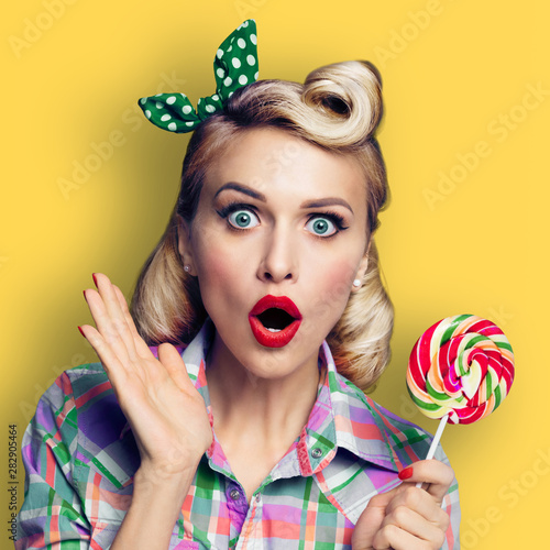 Photo of beautiful surprised woman with lollipop, dressed in pin-up style, yellow color background, square composition