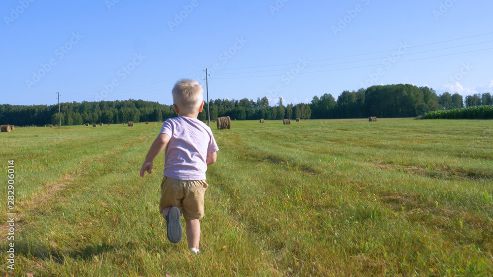 Cute little boy in shorts runs across the field and launches a toy airplane around a haystack and corn field. Concept of: Play, Summer, Field, Eco, Happy. Cute little boy in shorts runs across the field and launches a toy airplane around a haystack and corn field. Concept of: Play, Summer, Field, Eco, Happy.