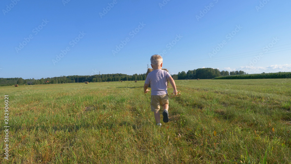 Cute little boy in shorts runs across the field and launches a toy airplane around a haystack and corn field. Concept of: Play, Summer, Field, Eco, Happy. Cute little boy in shorts runs across the field and launches a toy airplane around a haystack and corn field. Concept of: Play, Summer, Field, Eco, Happy.