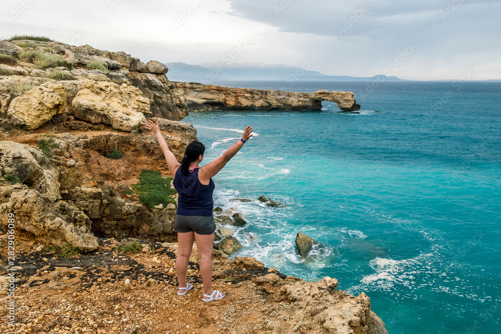 girl stands on the edge of a cliff with arms outstretched and looks into the distance at sea