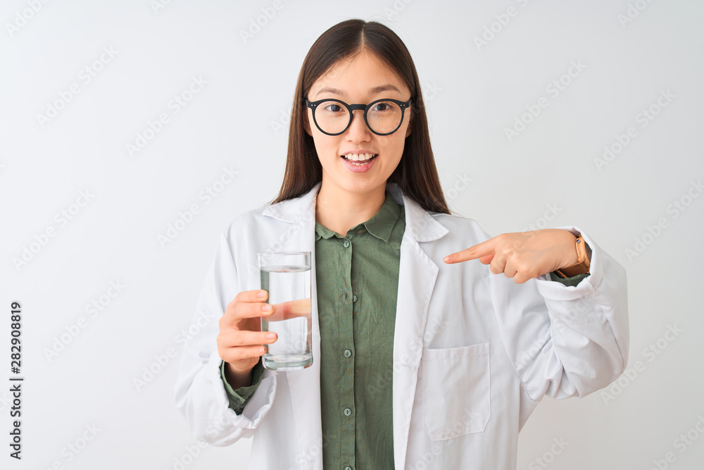 Young chinese dooctor woman wearing glasses drinking water over isolated white background with surprise face pointing finger to himself Young chinese dooctor woman wearing glasses drinking water over isolated white background with surprise face pointing finger to himself