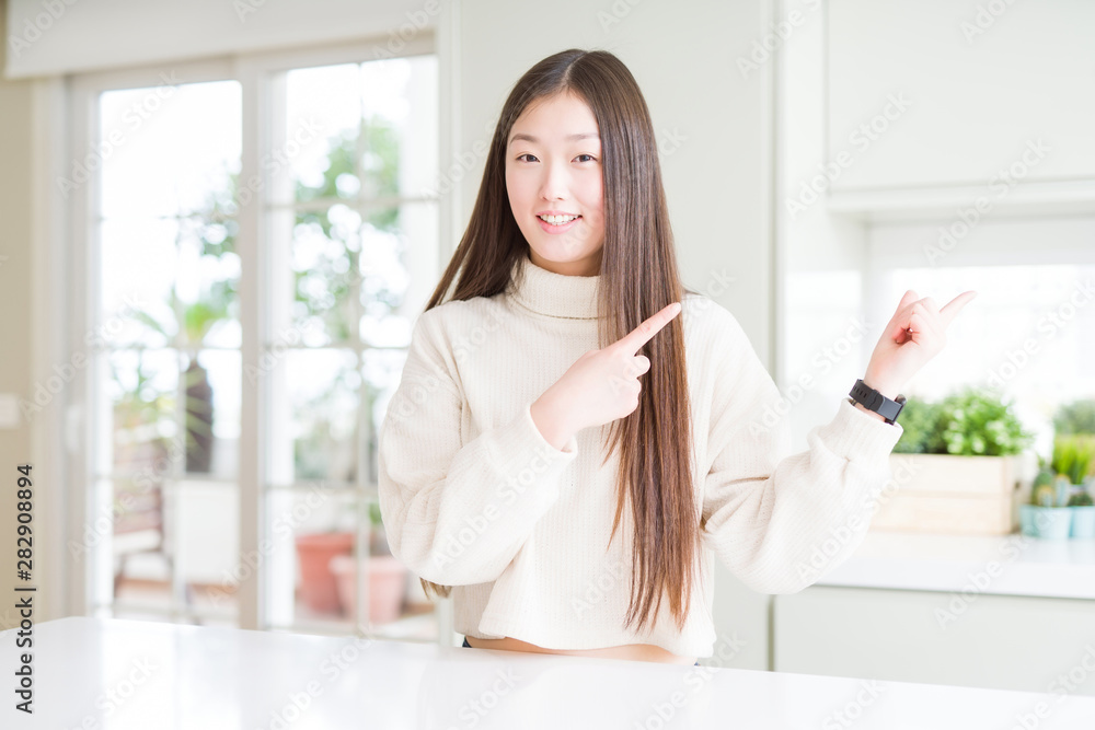 Beautiful Asian woman wearing casual sweater smiling and looking at the camera pointing with two hands and fingers to the side. Beautiful Asian woman wearing casual sweater smiling and looking at the camera pointing with two hands and fingers to the side.