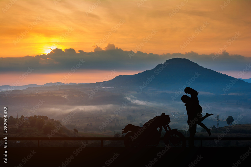 Couple silhouette kissing at sunset and have a big bike parked on the street,enjoying freedom and active lifestyle, having fun on a bikers tour on sunset background. Couple silhouette kissing at sunset and have a big bike parked on the street,enjoying freedom and active lifestyle, having fun on a bikers tour on sunset background.