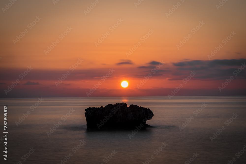 An amazing sunet behind a rock in a smooth sea.