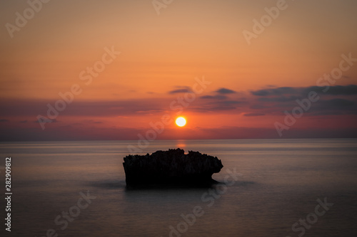 Obraz na płótnie An amazing sunet behind a rock in a smooth sea. w salonie