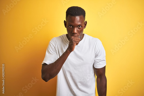 Young african american man wearing white t-shirt standing over isolated yellow background feeling unwell and coughing as symptom for cold or bronchitis. Healthcare concept.