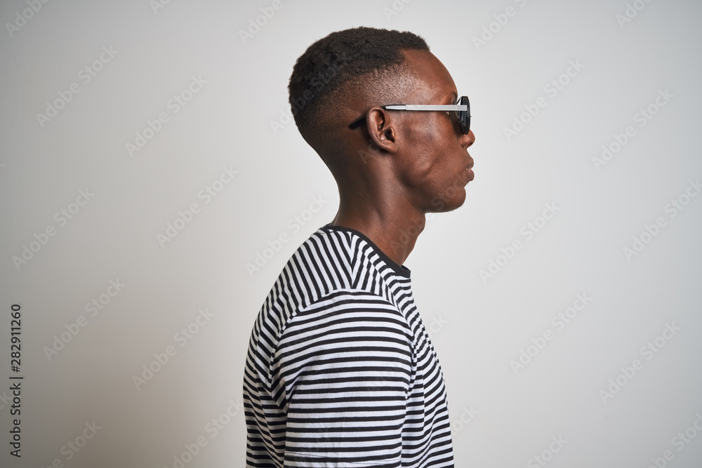 African american man wearing striped t-shirt and sunglasses over isolated white background looking to side, relax profile pose with natural face with confident smile. African american man wearing striped t-shirt and sunglasses over isolated white background looking to side, relax profile pose with natural face with confident smile.