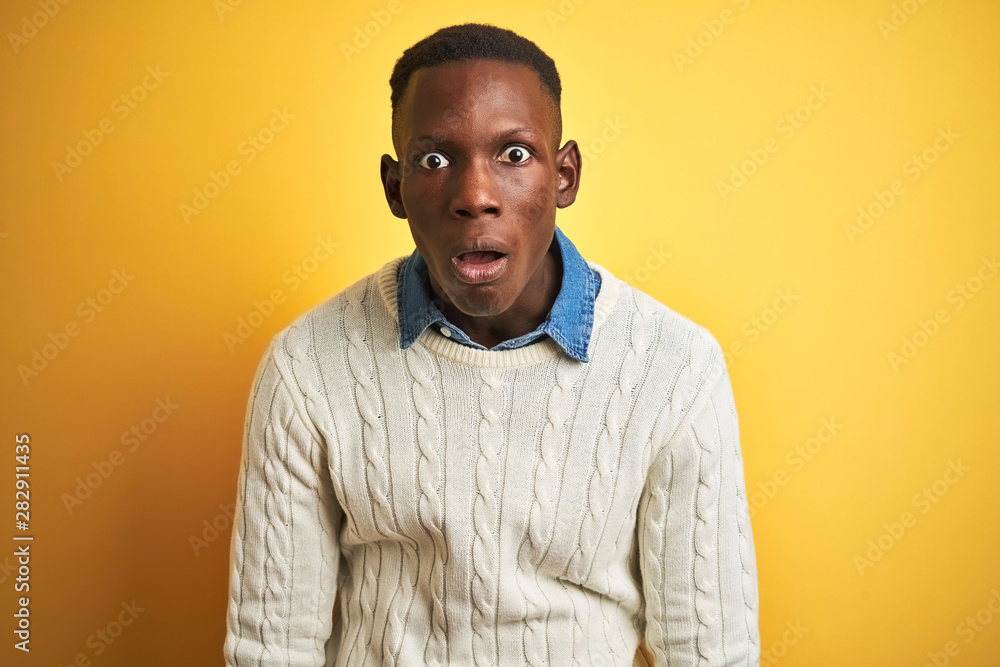 African american man wearing denim shirt and white sweater over isolated yellow background afraid and shocked with surprise and amazed expression, fear and excited face. African american man wearing denim shirt and white sweater over isolated yellow background afraid and shocked with surprise and amazed expression, fear and excited face.