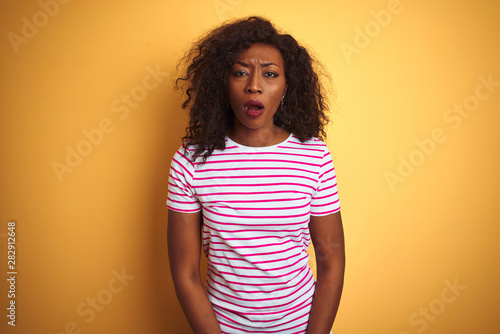 Young african american woman wearing striped t-shirt over isolated yellow background afraid and shocked with surprise expression, fear and excited face.