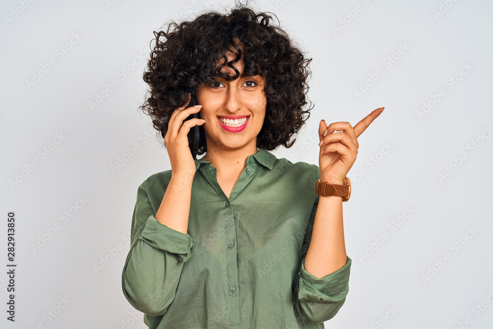 Young arab woman with curly hair talking on smartphone over isolated white background very happy pointing with hand and finger to the side Young arab woman with curly hair talking on smartphone over isolated white background very happy pointing with hand and finger to the side