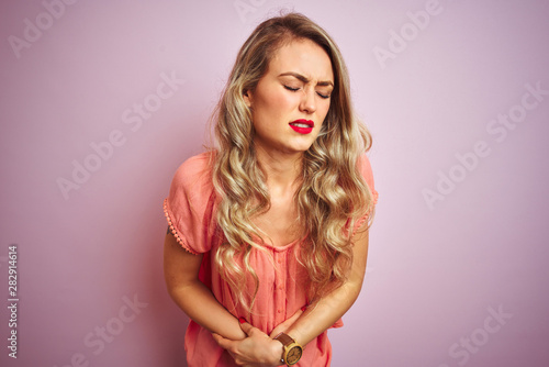 Young beautiful woman wearing t-shirt standing over pink isolated background with hand on stomach because indigestion, painful illness feeling unwell. Ache concept.