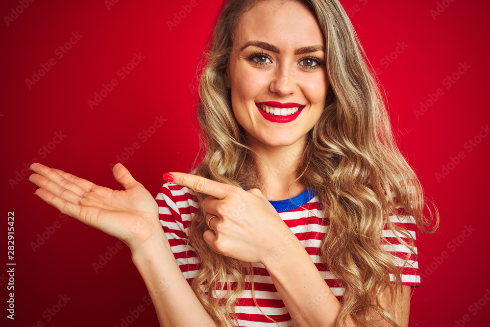 Young beautiful woman wearing stripes t-shirt standing over red isolated background very happy pointing with hand and finger Young beautiful woman wearing stripes t-shirt standing over red isolated background very happy pointing with hand and finger
