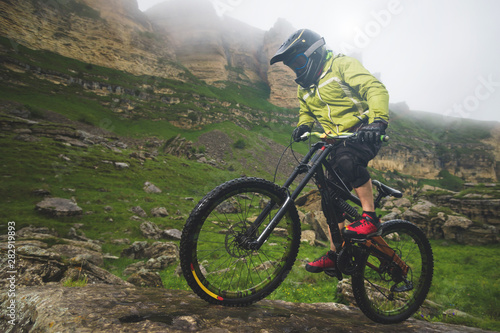 Side view wide angle partly a man on a mountain bike travels on rocky terrain Against the background of cloudy sky and epic rocks. The concept of a mountain bike and mtb downhill