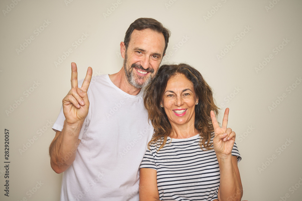 Beautiful middle age couple together standing over isolated white background smiling with happy face winking at the camera doing victory sign. Number two. Beautiful middle age couple together standing over isolated white background smiling with happy face winking at the camera doing victory sign. Number two.