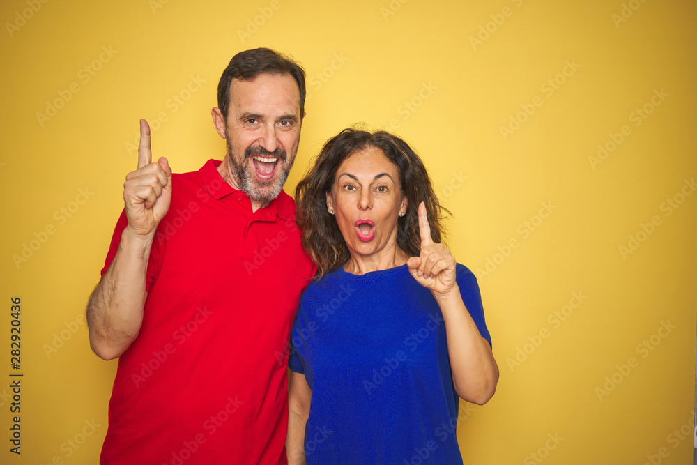 Beautiful middle age couple together standing over isolated yellow background pointing finger up with successful idea. Exited and happy. Number one. Beautiful middle age couple together standing over isolated yellow background pointing finger up with successful idea. Exited and happy. Number one.