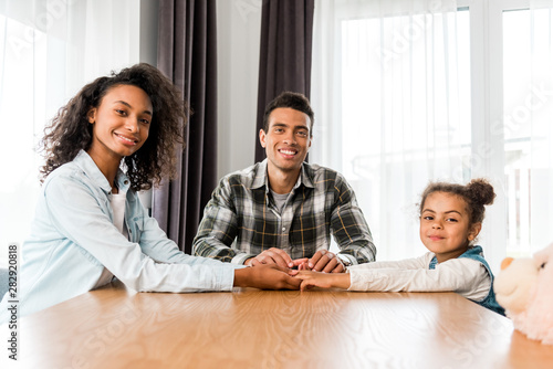 african american family sitting before table, smiling and looking at camera
