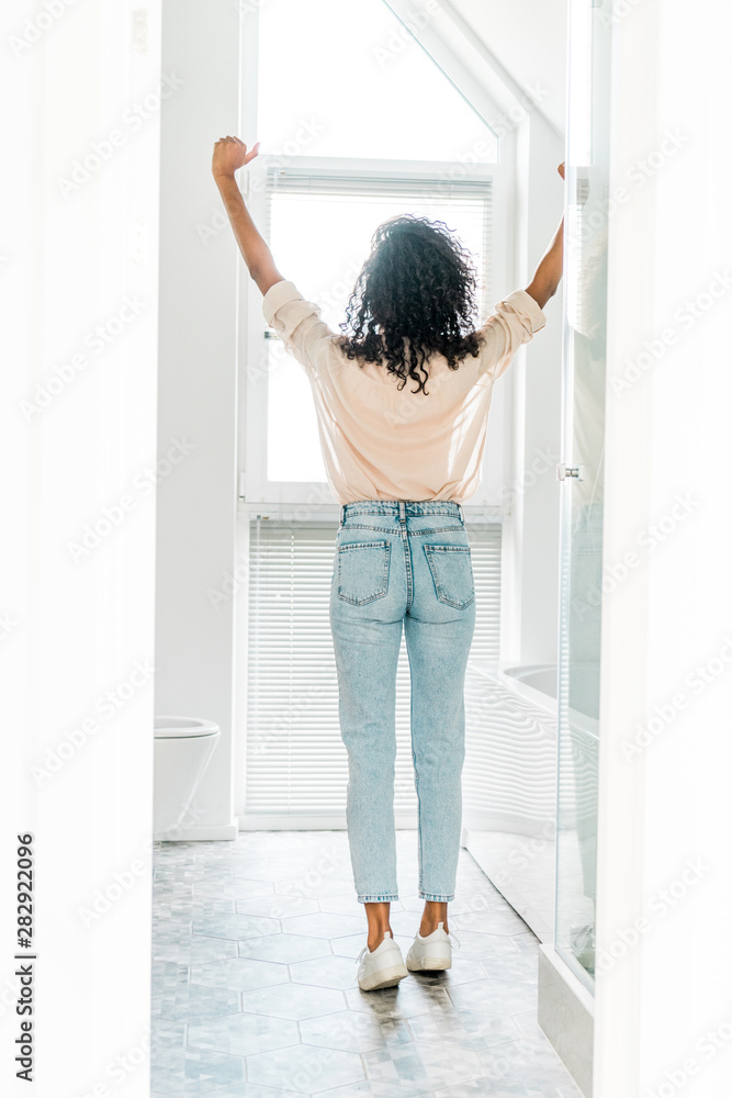 back view of woman standing in bathroom with hands in air back view of woman standing in bathroom with hands in air