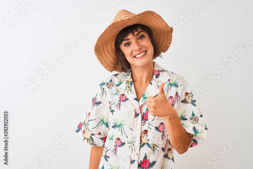 Beautiful woman on vacation wearing summer shirt and hat over isolated white background doing happy thumbs up gesture with hand. Approving expression looking at the camera with showing success.